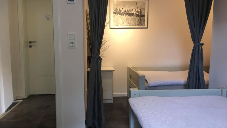 A simple room with two beds and a window. Curtains separate the space, and a black-and-white photo hangs on the wall.