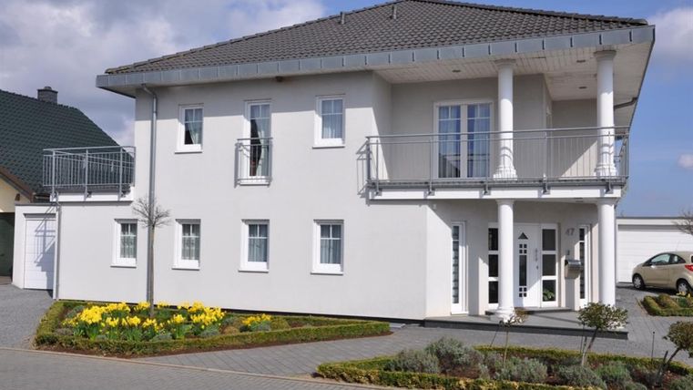 A modern, two-story house with a gray roof and large windows. The front yard is designed with yellow flowers and a narrow path.