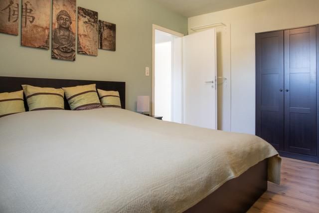 Ein gemütliches Schlafzimmer mit einem großen Bett und dekorativen Kissen. An der Wand hängen interessante Kunstwerke und es gibt einen Kleiderschrank in der Ecke.