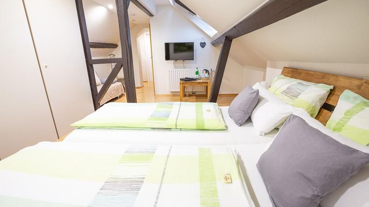 A cozy bedroom with two beds decorated with bright, striped bedding. The wooden ceiling and the television in the background create an inviting atmosphere.