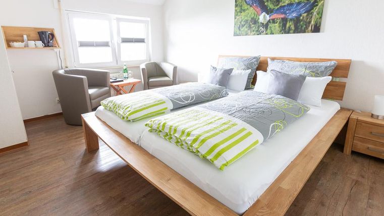 A modern bedroom with a large double bed and colorful pillows. In the corner, there are two cozy armchairs and a table.
