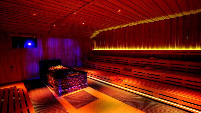 A relaxing sauna with wooden-paneled walls and soft lighting. The atmosphere is calm and inviting.