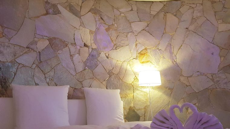 A cozy bedroom with a large bed and soft pillows. The rounded stone wall and gentle lighting create a relaxing atmosphere.