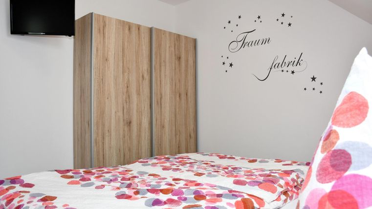 Een gezellig slaapkamer met een bed en kleurrijke kussens. Aan de muur staat de tekst "Droomfabriek" en er is een televisie.