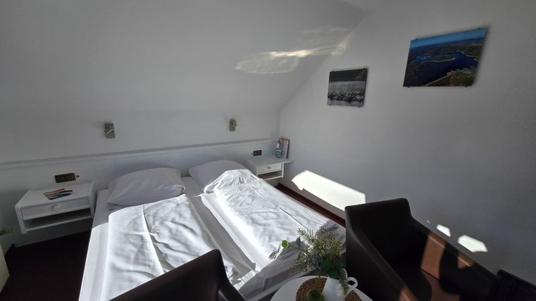 A cozy room with two beds and modern design. There is a small table with a flower vase and comfortable chairs.