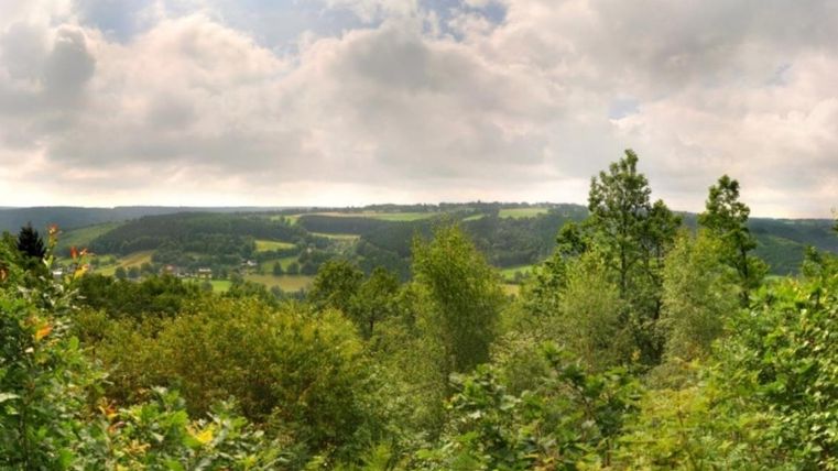 A picturesque landscape with green trees and gentle hills. The sky is cloudy, creating a serene atmosphere.