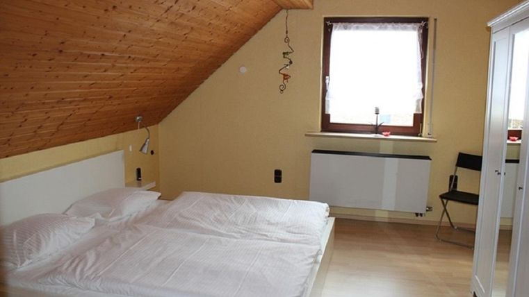 A cozy bedroom with a double bed and a window. The walls are in warm colors, and the ceiling has wooden paneling.