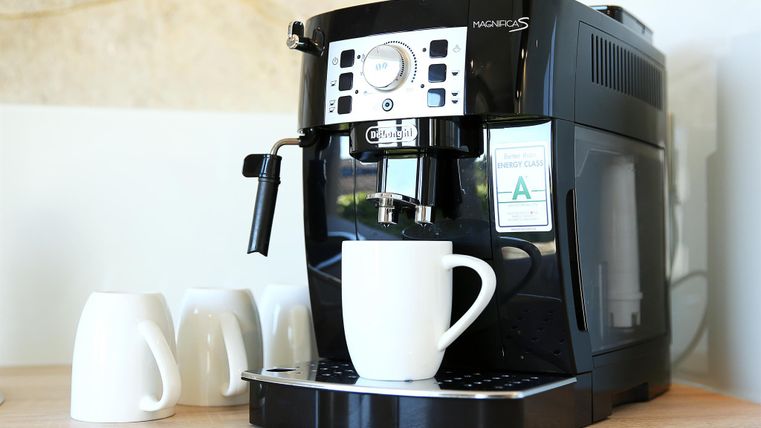 A coffee machine is on a table with a white cup underneath. Next to it are several white cups.