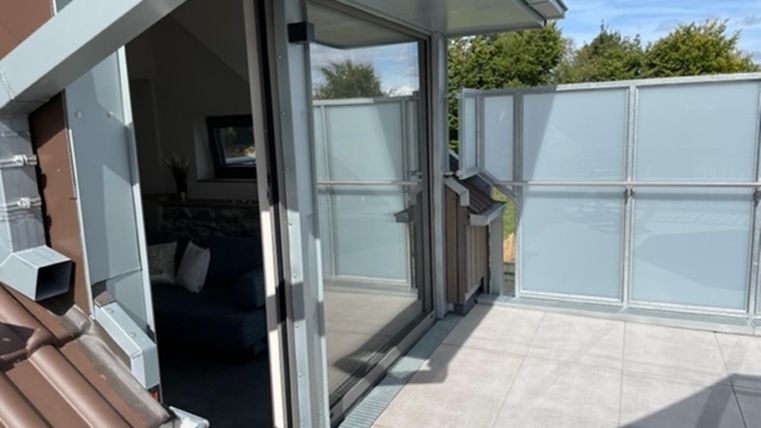 Een modern balkon met glazen balustrade en een prachtig uitzicht. De open deuren leiden naar de binnenkant van de ruimte.