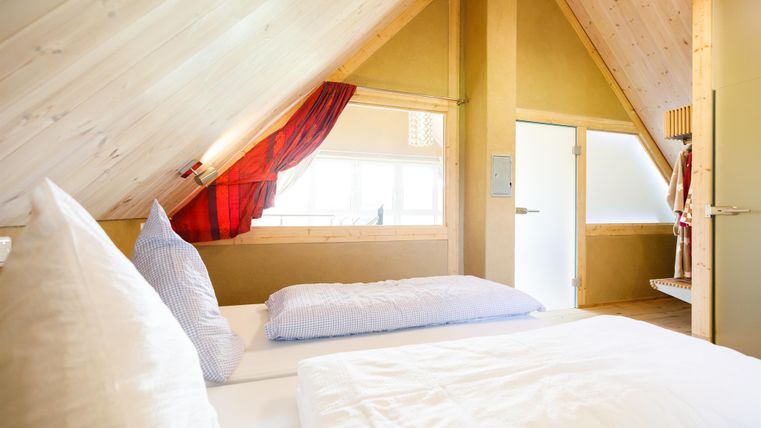 A cozy bedroom with sloped walls and wood paneling. The atmosphere is bright and inviting, with large windows and modern furniture.