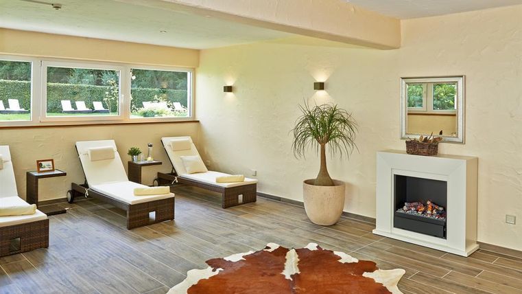 Ein entspannender Wellnessbereich mit Liegen und großen Fenstern. Ein moderner Kamin sorgt für eine gemütliche Atmosphäre.