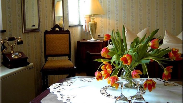 Ein gemütliches Zimmer mit einem Tisch, auf dem eine Vase mit bunten Tulpen steht. Im Hintergrund sind eine Lampe und ein Stuhl zu sehen.