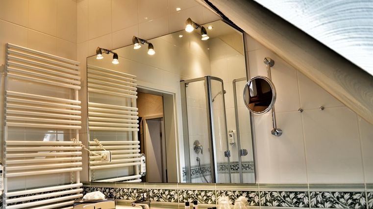A modern bathroom with a sink and a large mirror. The walls are brightly tiled, and there is a shower as well as towel racks.