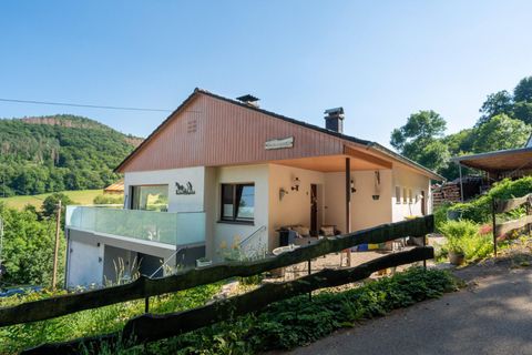 A modern house in a rural setting with a glass veranda. In the background, green hills and trees can be seen.