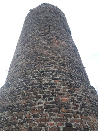 A historical stone building that rises high into the sky. The tower has a rustic structure made of bricks and is surrounded by a gray cloud landscape.