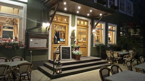 Een uitnodigend restaurant met houten bekleding en verlichte vensters. Voor de ingang staan tafels en stoelen voor gasten buiten.