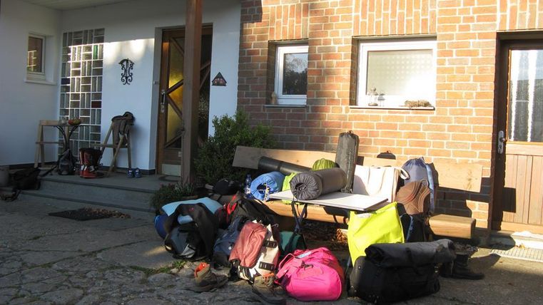 A collection of backpacks and luggage lies in front of an entrance. The area is brightly lit and gives an inviting impression.