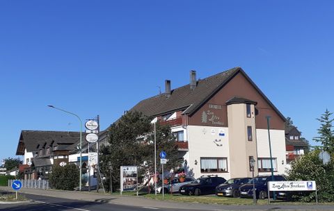 A cozy hotel building with a mix of modern and traditional elements. In front of the hotel, several cars are parked, and in the background, more buildings can be seen.