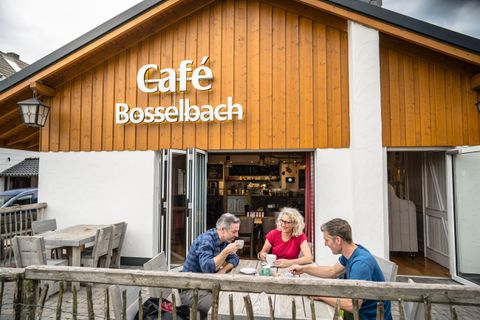 A cozy café called "Café Bosselbach." Three people are enjoying their time outside at a table.