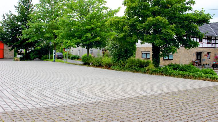 Een lege plaats met een betegelde vloer en enkele bomen. Op de achtergrond zijn gebouwen te zien.