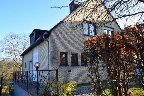 A charming house with a brick facade and large windows. The garden is designed with trees and bushes.