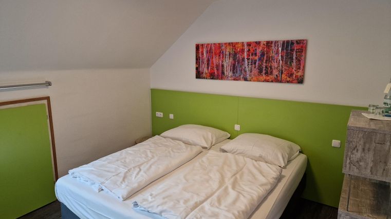 A cozy bedroom with a double bed and a modern green wall. A colorful artwork hangs on the wall, decorating the space.