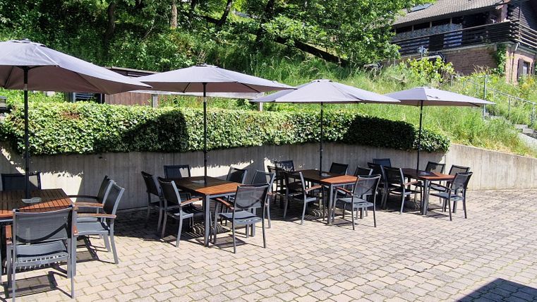 A cozy outdoor area with tables and umbrellas. Surrounded by green plants and an inviting atmosphere.