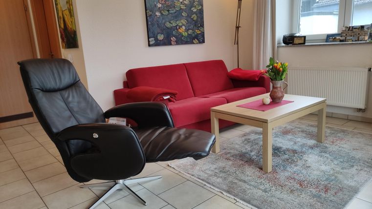 A cozy living room with a red sofa and a black swivel chair. On the table is a vase with flowers and a painting hangs in the background.