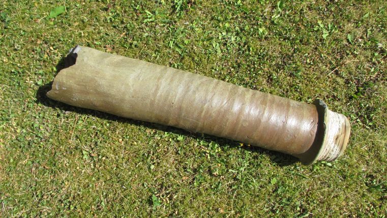 Ein langer, zylindrischer Gegenstand liegt auf grünem Gras. Er hat eine glatte Oberfläche und eine abgerundete Endseite.