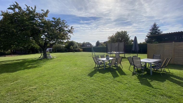 Een mooie tuin met groen gras en een grote boom. Er staan meerdere tafels en stoelen in het midden van de tuin.