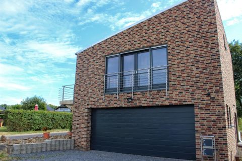 Een modern, twee verdiepingen tellend huis van baksteen met grote ramen. Voor het gebouw bevindt zich een garage en de lucht is helder en blauw.