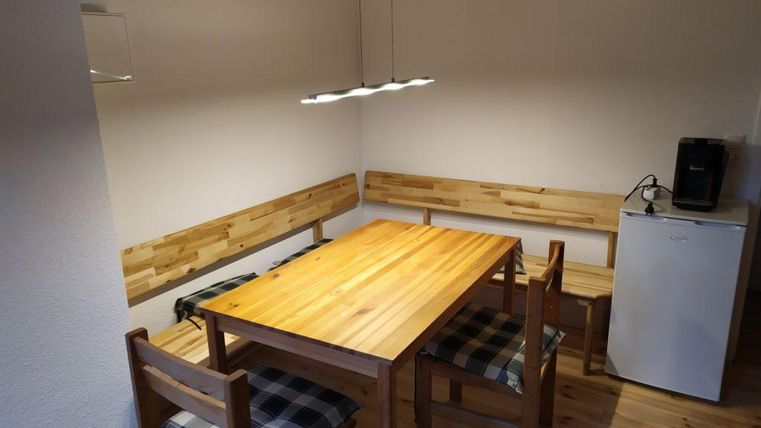 A cozy dining area with a wooden table and chairs. Along one wall, there are benches and a refrigerator in the corner.