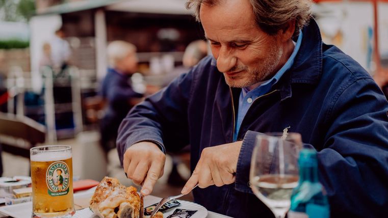A man is sitting at a table and enjoying his meal. In front of him are a beer and a glass of wine.
