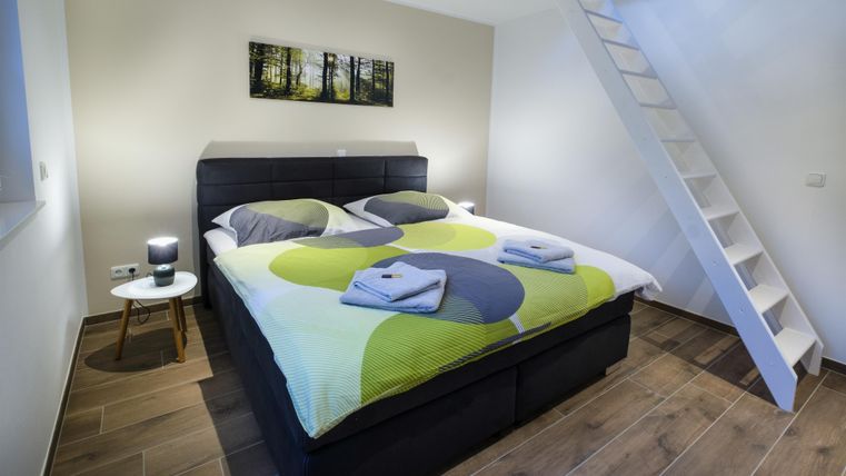 Een moderne slaapkamer met een groot bed, kleurrijke beddengoed en een klein nachttafeltje. Een trap leidt naar een hoger gedeelte van de kamer.