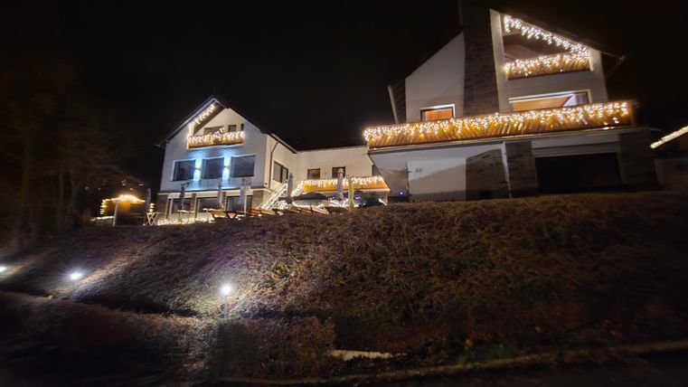 A modern house with festive lighting at night. The lights illuminate the facade and surrounding areas.