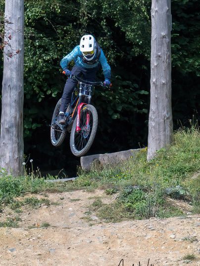 A cyclist jumps over a ramp in the woods. The rider is wearing a helmet and tight clothing.