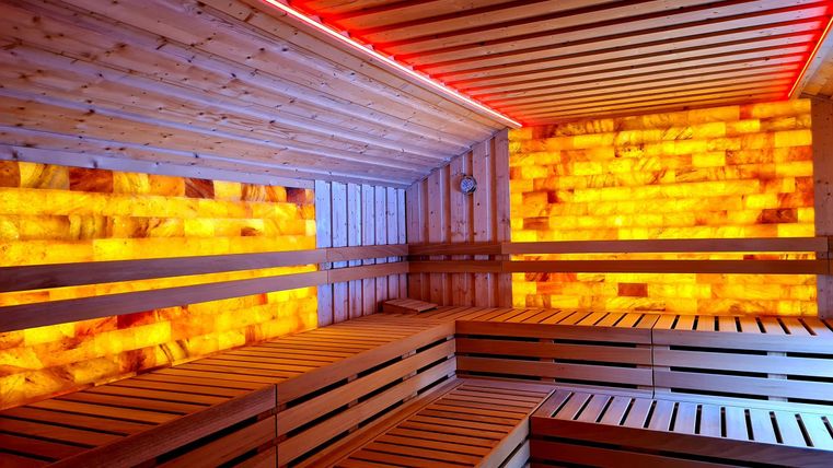 A modern sauna interior with wooden loungers and soft lighting. The walls are designed with colored salt crystals.
