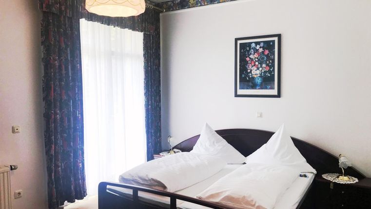 Een gezellige slaapkamer met een tweepersoonsbed en twee kussens. Grote ramen laten veel daglicht binnen en de ruimte is smaakvol ingericht.
