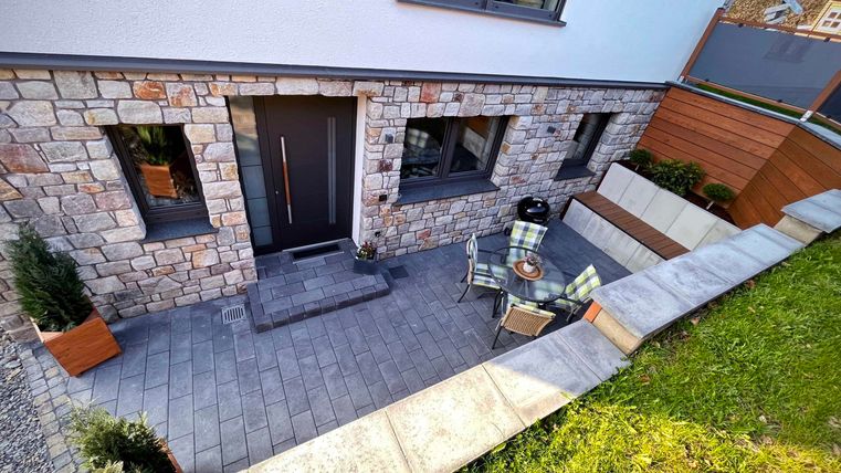 A modern entrance area with a stone facade. In front of the door, there is a small seating area with a table and chairs.