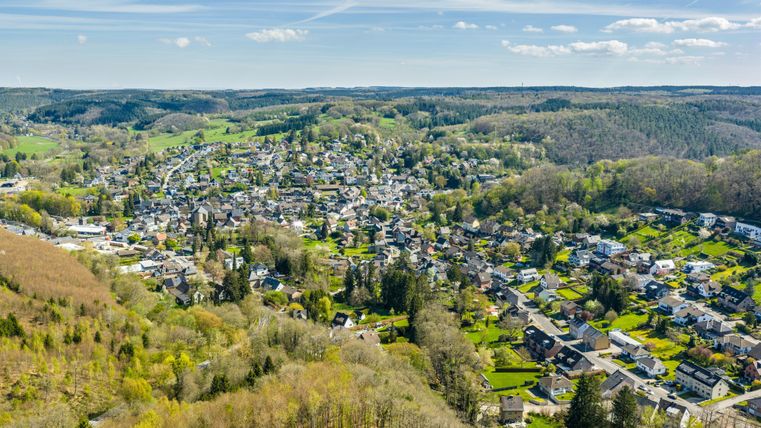 Eine malerische Aussicht auf ein ruhiges Dorf umgeben von grünen Hügeln und Wäldern. Die Häuser sind gut verteilt und die Landschaft wirkt einladend und friedlich.