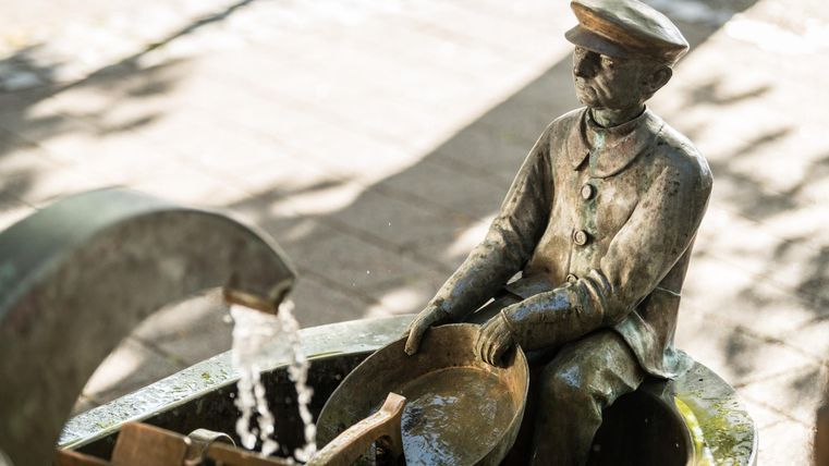 A statue of a man in uniform with a shovel in his hands. Water flows from a nearby spring.