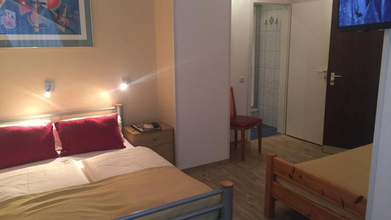 Een eenvoudige kamer met twee bedden, een televisie en een kleine tafel. De muren zijn licht en er is een kunstwerk boven het bed.