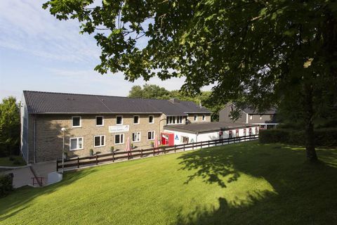 A modern building surrounded by green spaces. There is a well-maintained lawn and some trees that provide shade.