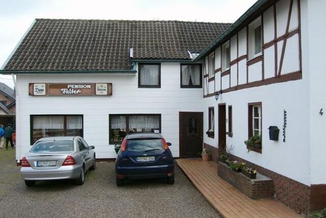 A guesthouse with a mix of modern and traditional architectural styles.
Two cars are parked in front of the entrance on a paved path.