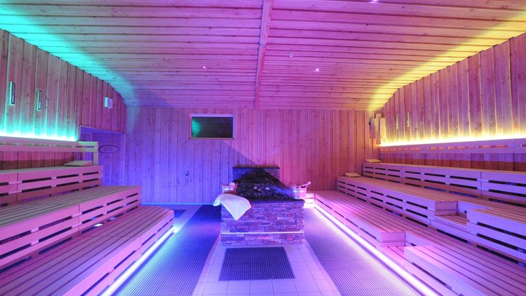 A modern sauna with a wooden bench and colorful LED lights. The room radiates a relaxing atmosphere.