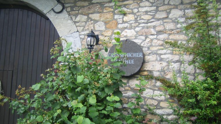 Ein historisches Steingebäude mit einer Holztür und einer auffälligen Wandlampe. Über dem Eingang hängt ein Schild mit der Aufschrift "Cress-picher Mühle".