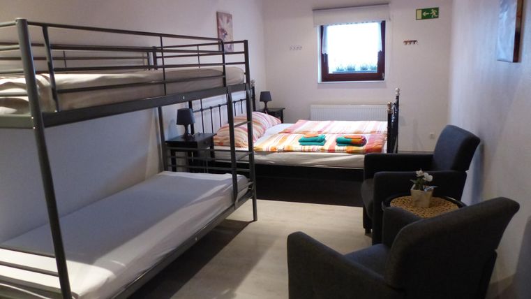 A room with a bunk bed and a double bed. There is also an armchair and a small table.