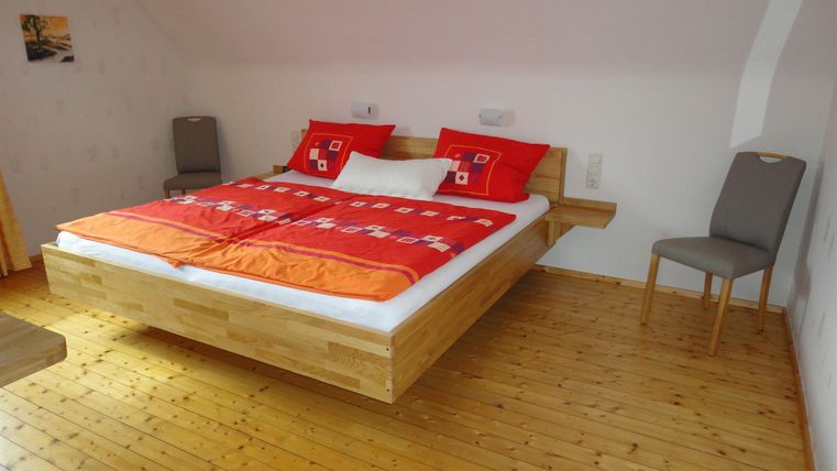 Een moderne slaapkamer met een groot houten bed en kleurrijke kussens. De vloer is van hout en er staat een stoel naast het bed.