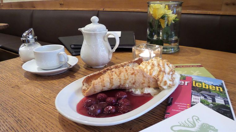 Een heerlijke crêpe met kersen op een wit bord. Op de achtergrond zijn een theepot en een bloem in een vaas te zien.