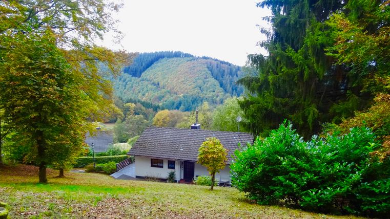 Ein gemütliches Haus in der Natur, umgeben von Bäumen und Hügeln. Die Landschaft ist im herbstlichen Farbenspiel.